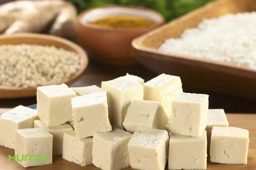 Kostki domowego tofu na drewnianej desce obok soi