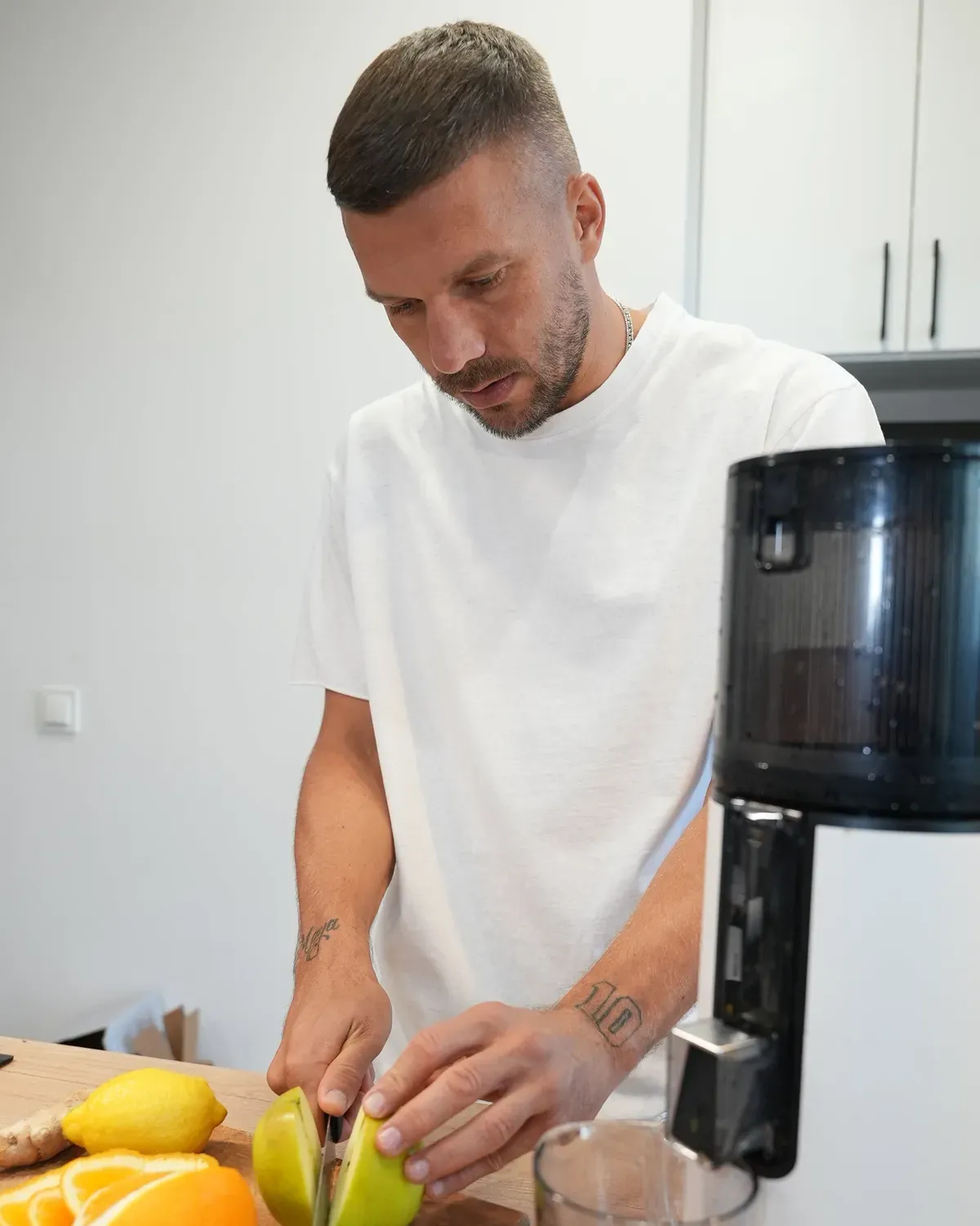 Lukas Podolski kroi owoce na desce obok białej wyciskarki Hurom