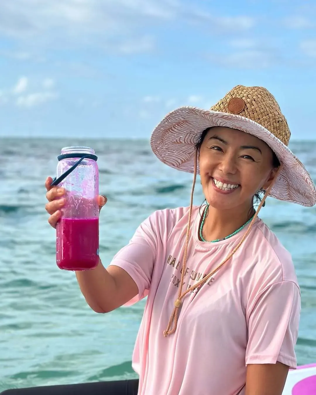Ritsuko Tanaka w kapeluszu z różowym sokiem w butelce na desce SUP na morzu