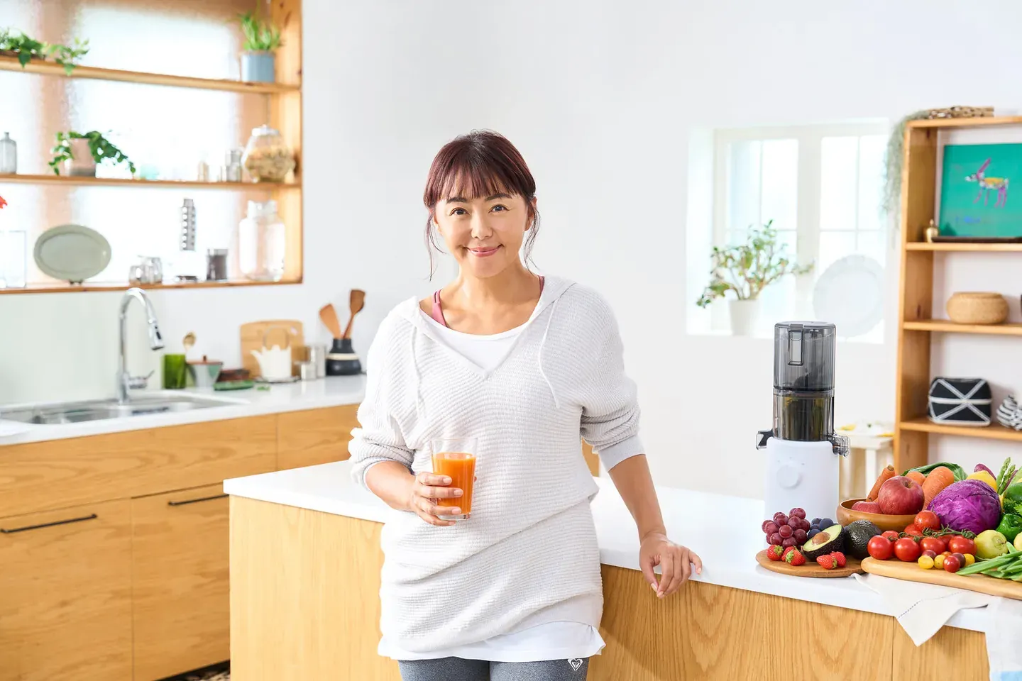 Ritsuko Tanaka ze szklanką soku w kuchni, obok wyciskarka Hurom i kolorowe warzywa